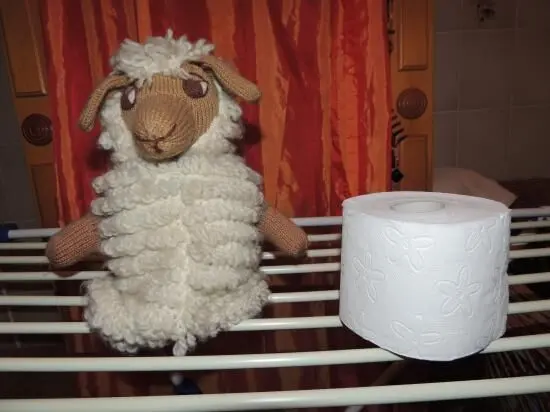 Eine Handpuppe in Schafgestalt steht neben einer Rolle Toilettenpapier auf einem Gestell in einem Badezimmer.