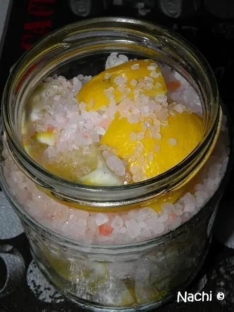 Ein Glas mit eingelegten Zitronen, gefüllt mit grobem Salz, steht auf einer dunklen Oberfläche.