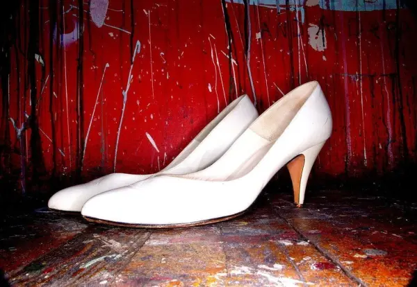 Weiße Schuhe stehen auf einem Holzfußboden, während die rote, fleckige Wand im Hintergrund auffällt.
