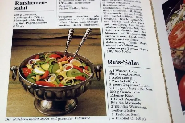 Ein eleganter Salat in einer silbernen Schüssel wird präsentiert, während die Zutaten frisch und bunt aussehen. Text beschreibt Rezepte.