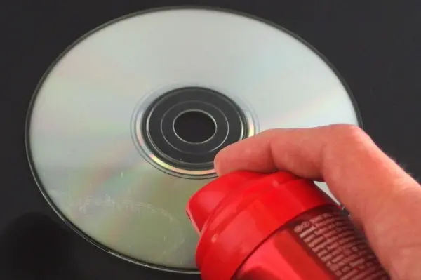 Ein Hand hält eine rote Sprühdose über eine glänzende CD, während Haarspray auf die CD aufsprüht.