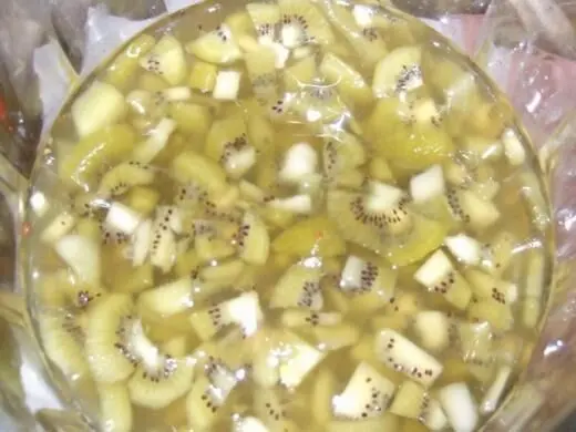 Eine Schüssel Kiwi-Bowle gefüllt mit geschnittenen Kiwi-Stücken in klarer Flüssigkeit, glänzend im Licht.