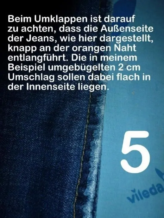 Ein Jeansstoffstück zeigt eine orange Naht, während Anweisungen zum Umklappen und Kürzen ohne Schere gegeben werden. Text: "Beim Umklappen ist darauf zu achten, dass die Außenseite der Jeans, wie hier dargestellt, knapp an der orangen Naht entlangführt. Die in meinem Beispiel umgebügelten 2 cm Umschlag sollen dabei flach in der Innenseite liegen."