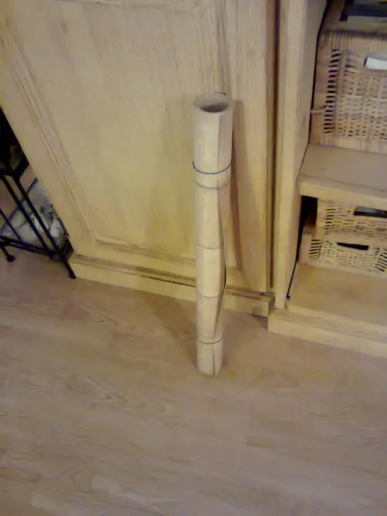 Ein aufrecht stehender Stoffrollenträger aus Holz steht auf einem hellen Boden, umgeben von einem Holzschrank.