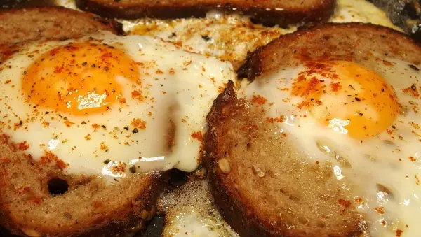 Gebratenes Brot mit Ei liegt in einer Pfanne, während das Ei brät und die Ränder goldbraun sind.