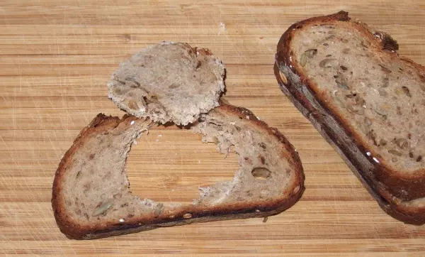 Ein Stück gebratenes Brot mit einem Loch in der Mitte liegt auf einem Holzbrett, als Vorbereitung für ein Ei.
