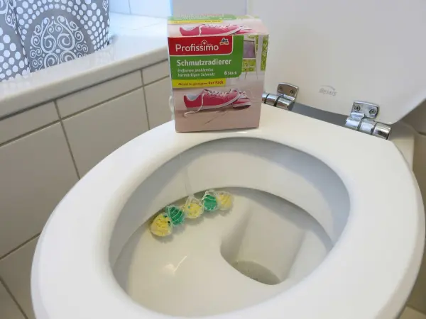 Ein Schmutzradierer liegt auf einem Toilettenrand, während bunte Reinigungsschwämme im WC schwimmen, um Urinstein zu entfernen.