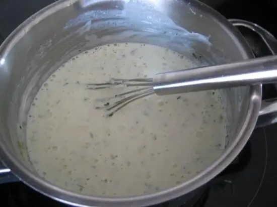In einem Topf wird eine cremige Schmand-Lachssauce mit einem Schneebesen gerührt, um eine köstliche Konsistenz zu erreichen.