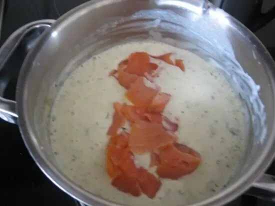 Eine metallene Schüssel zeigt eine cremige Schmand-Lachssauce mit Lachsstreifen, die sanft darin schwimmen.