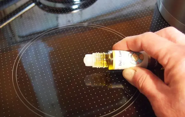 Ein Hand hält eine Flasche ätherisches Öl, während es auf ein Kochfeld aufgetragen wird, um unangenehme Kochgerüche zu beseitigen.
