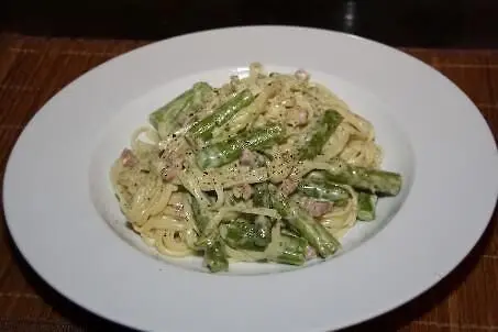 Ein Teller Linguine mit grünem Spargel ist dekorativ angerichtet, umgeben von einem neutralen Hintergrund.
