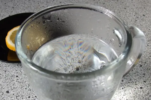 Ein Glas heißes Wasser steht auf einem Tisch, während es dampft. Nebenbei liegt eine Zitronenscheibe.