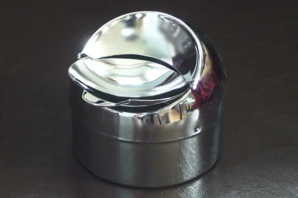 Ein glänzender Aschenbecher aus Metall steht auf einer dunklen Oberfläche, bereit zum Einsatz für saubere Rauchergewohnheiten.