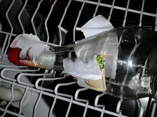 Eine Marmeladenglasflasche liegt in einem Geschirrspüler und hat ein angefeuchtetes Küchenpapier um den Etikett-Bereich gewickelt.