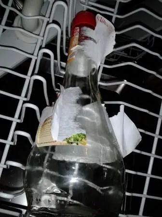 Eine Flasche steht in einem Geschirrspüler, die Etiketten blättern ab und sie ist teilweise mit Wasser bedeckt.