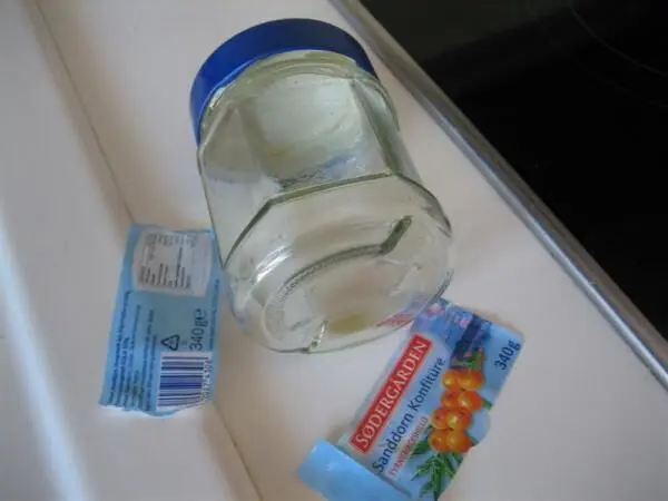 Ein Glas Marmelade steht auf einer weißen Fläche, während sich die Etiketten daneben lösen und abfallen.