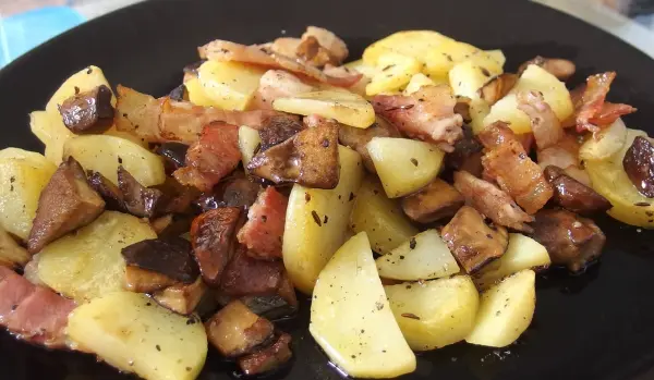 Gebratene Pilze und Kümmel-Speck-Kartoffeln liegen appetitlich auf einem schwarzen Teller, dampfend in einer Küche serviert.