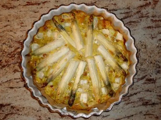 Eine goldbraune Kartoffel-Spargel-Tortilla aus dem Backofen liegt in einer runden Form auf einem hellen Tisch.