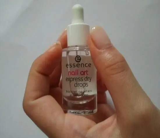 Eine Hand hält eine kleine Flasche mit Pipette. Auf dem Etikett steht: "essence nail art express dry drops trocknet nagellack".