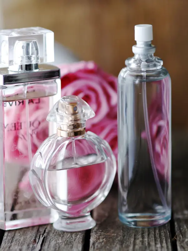 Drei Parfümflaschen stehen auf einem Holztisch, umgeben von rosa Rosenblüten, die den Duft vom Lieblingsparfum im Deo unterstreichen.