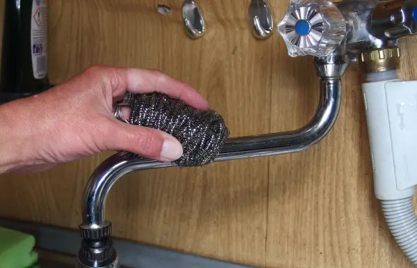 Eine Hand reinigt eine verkalkte Armatur mit einem Scheuerschwamm, um Ablagerungen in der Küche zu entfernen.