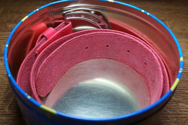 Ein rosa Gürtel liegt ordentlich in einer runden, bunten Dose, die als Aufbewahrungsort dient.