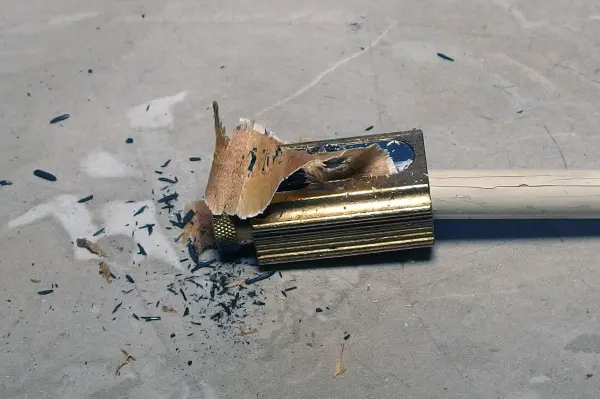 Ein abgebrochener Holzgriff liegt auf einer glatten Oberfläche, umgeben von Holz- und Graphitspänen, die Motten vertreiben.