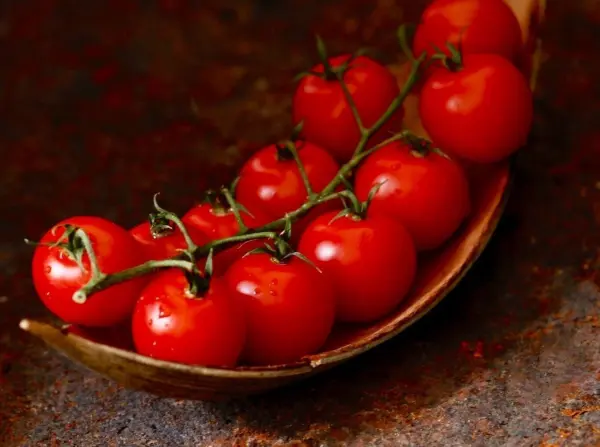 Saftige, rote Tomaten liegen auf einem metallenen Löffel, bereit für das Chutney-Rezept mit Senf-Saat in der Küche.