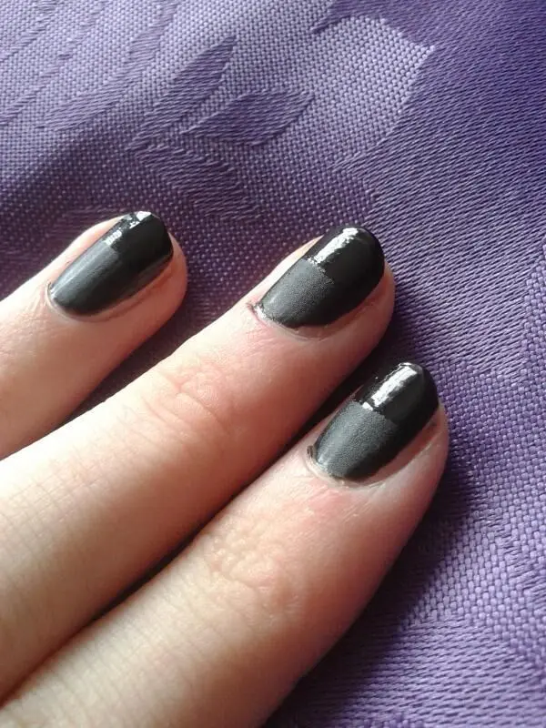 Schwarzer matter Nagellack bedeckt Fingernägel auf violettem Stoffhintergrund, der Textur und Tiefe zeigt.