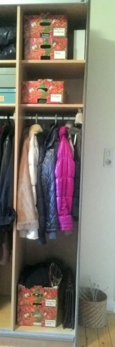 Eine dekorative Obstkiste steht im Schrank und organisiert Jacken, während der Raum neutral und ordentlich wirkt.
