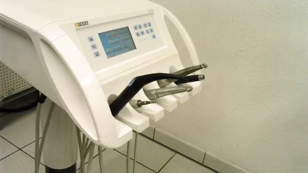 Ein Zahnarztstuhl mit Geräten steht bereit, um Patienten zu helfen. Die Umgebung ist hell und klinisch.