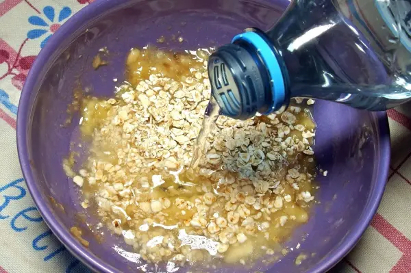 In einer lila Schüssel wird Wasser auf eine Mischung aus Bananen und Haferflocken gegossen, um Bananen-Hafer-Schleim für die Magenberuhigung herzustellen.