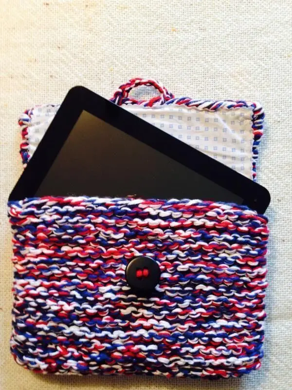 Eine bunte, gestrickte Tablet-Tasche liegt offen da, während ein schwarzes Tablet darin fast herausragt.