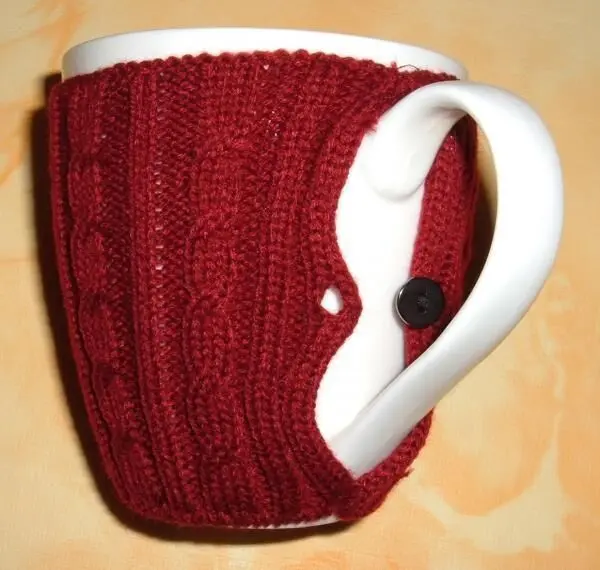 Ein roter Pulli für die Kaffeetasse umhüllt die Tasse, die eine warme Atmosphäre in einer gemütlichen Umgebung schafft.