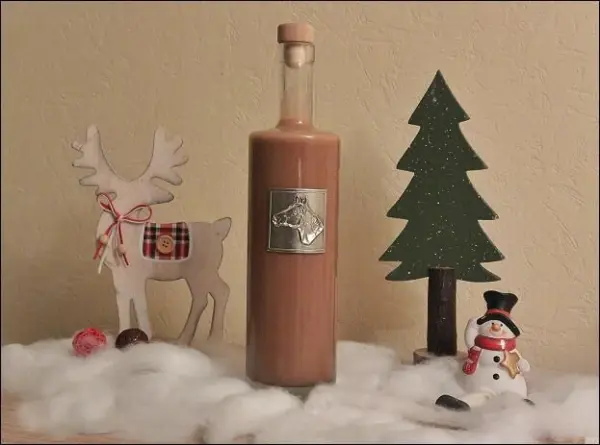 Eine Flasche Lebkuchen-Likör steht zwischen einem Rentier und einem Weihnachtsbaum auf einer weißen, winterlichen Unterlage.