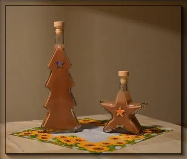 Zwei Flaschen, eine in Form eines Tannenbaums und die andere als Stern, stehen auf einem Tisch und präsentieren Lebkuchen-Likör.