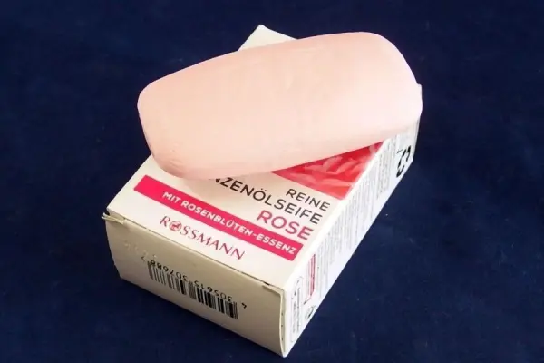 Ein rosa Seifenstück liegt auf einer weißen Verpackung mit rotem Text, umgeben von einem dunklen Hintergrund.
