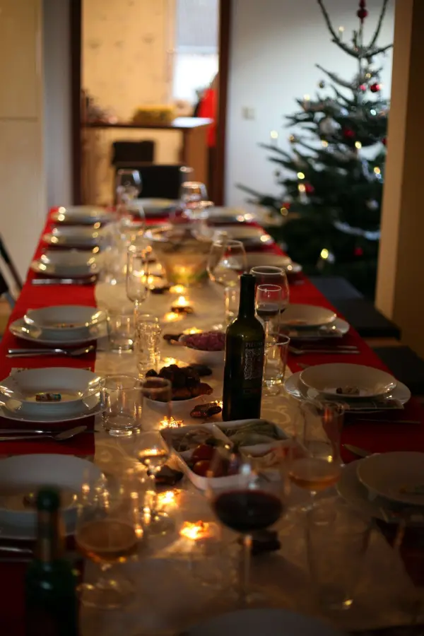 Ein festlich gedeckter Tisch mit Wein und Plätzchen strahlt in einem gemütlichen Raum, während ein Weihnachtsbaum leuchtet.