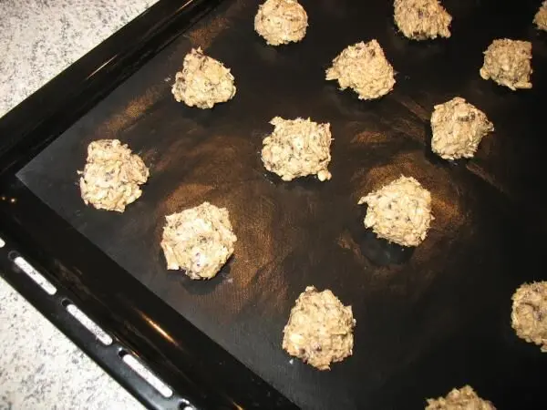 Schokoladen-Haferflocken-Cookies mit Sonnenblumenkernen sind in kleinen Portionen auf einem Blech angeordnet und bereit zum Backen.