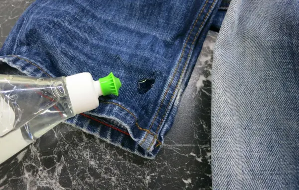 Eine Flasche Spülmittel steht auf dem Hosenbein einer Jeans, um einen Ölfleck vorzubehandeln.