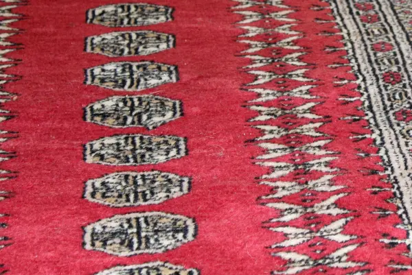 Ein roter Teppich mit grafischen Mustern zeigt einen Rotweinfleck. Der Fleck sitzt prominent auf dem Teppich.