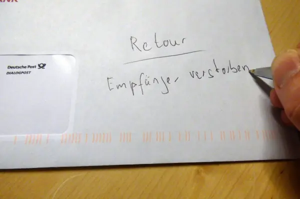 Eine Hand hält einen Stift und schreibt auf einen Briefumschlag, der für ein Werbeschreiben verwendet wird.