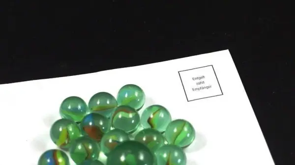 Eine Ansammlung grüner Murmeln liegt auf einem weißen Blatt Papier, das auf einem schwarzen Hintergrund platziert ist.