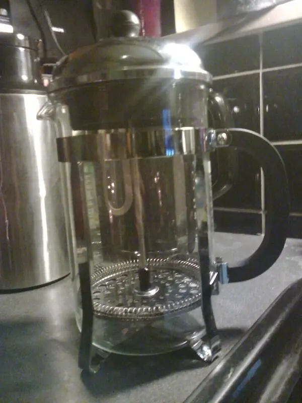 Eine leere French Press steht auf einer Küchenarbeitsplatte mit Fliesen im Hintergrund.