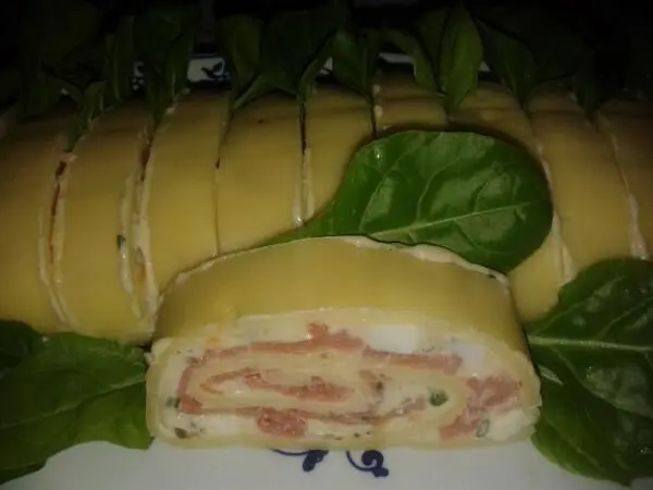 Eine Käse-Lachs-Rolle auf frischen Blättern zeigt, wie die appetitliche Füllung in der Rolle sichtbar ist.