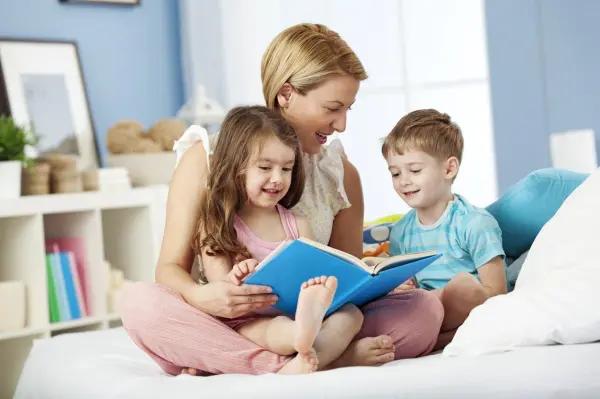 Eine Mutter liest mit ihren zwei Kindern in einem hellen Raum ein Buch; eine liebevolle, entspannte Atmosphäre fördert das Gespräch über Probleme.