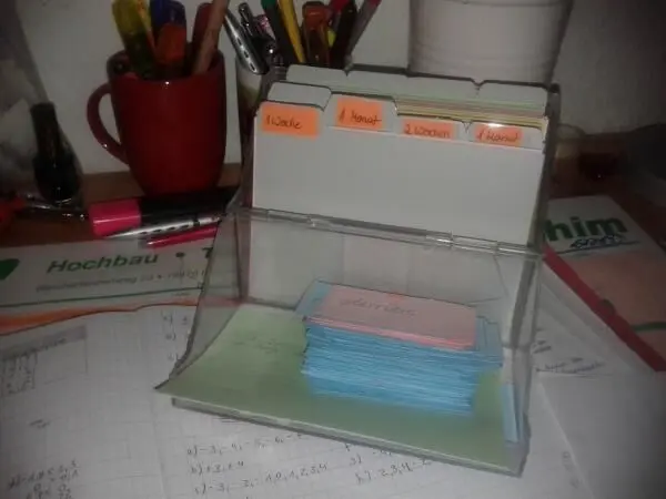 Ein Karteikartensystem auf einem Schreibtisch enthält Karten, die in Fächer nach Zeiten sortiert sind: 1 Woche, 1 Monat, 2 Wochen, 3 Monate.