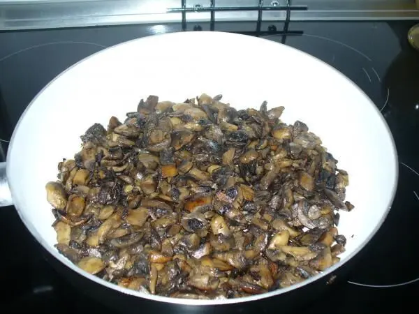 Gebratene Champignons füllen eine weiße Schüssel, während sie auf einem Herd zum Einfrieren vorbereitet werden.