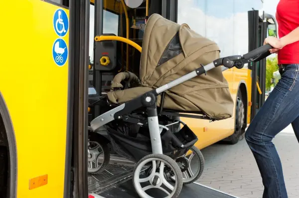 Ein Kinderwagen wird in einen gelben Bus geschoben, während eine Person ihn sicher hineinschiebt, um unterwegs zu reisen.
