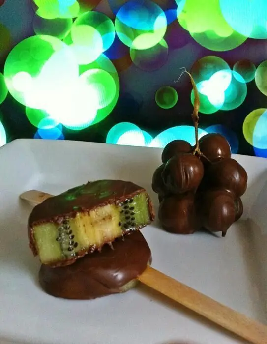 Ein Schoko-Kiwi Lutscher liegt auf einem Teller, während bunte Lichter im Hintergrund leuchten, die ein festliches Ambiente schaffen.